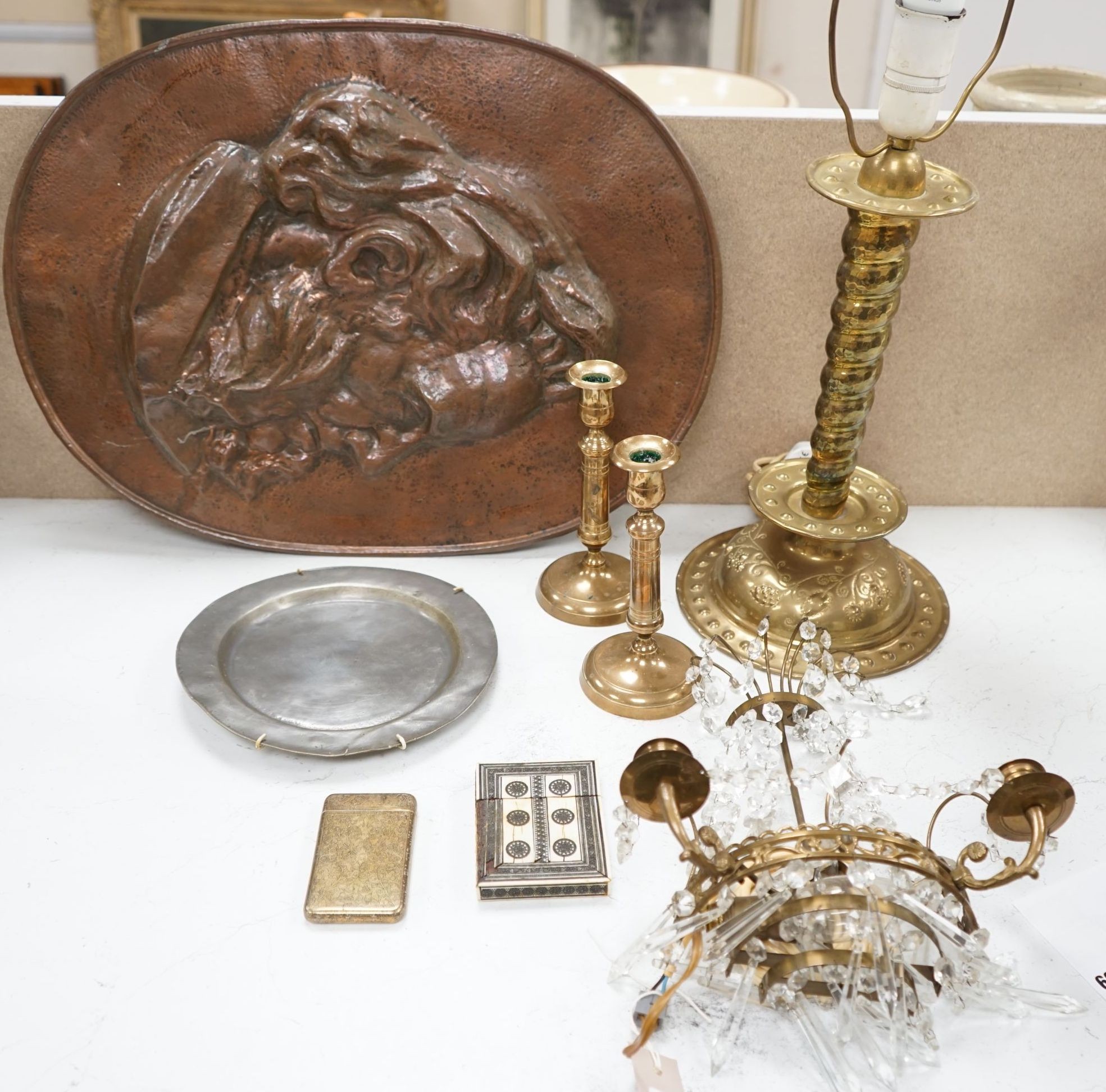 An embossed brass lamp, lustre drop wall light, a pair of bell-metal candlesticks, an 18th century pewter plate and a large Swedish embossed plaque